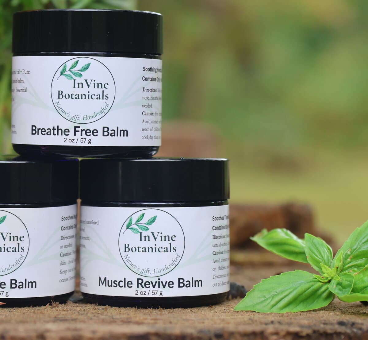Jars of InVine Muscle Revive Balm and Breathe Free Balm on a wood stump with fresh basil, a natural alternative to Biofreeze